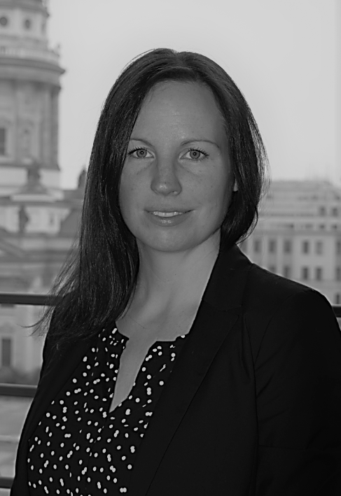 Woman in blazer smiles, city background.
