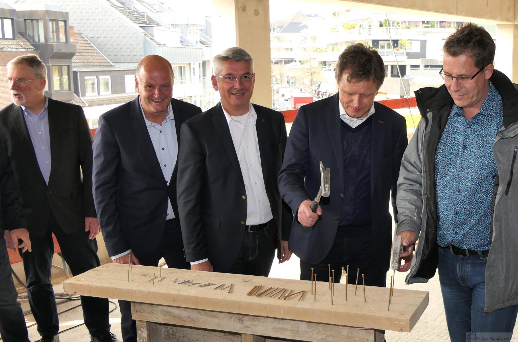 Männer auf einer Baustelle schlagen Nägel in ein Holzbrett mit der Aufschrift „Hesss“.