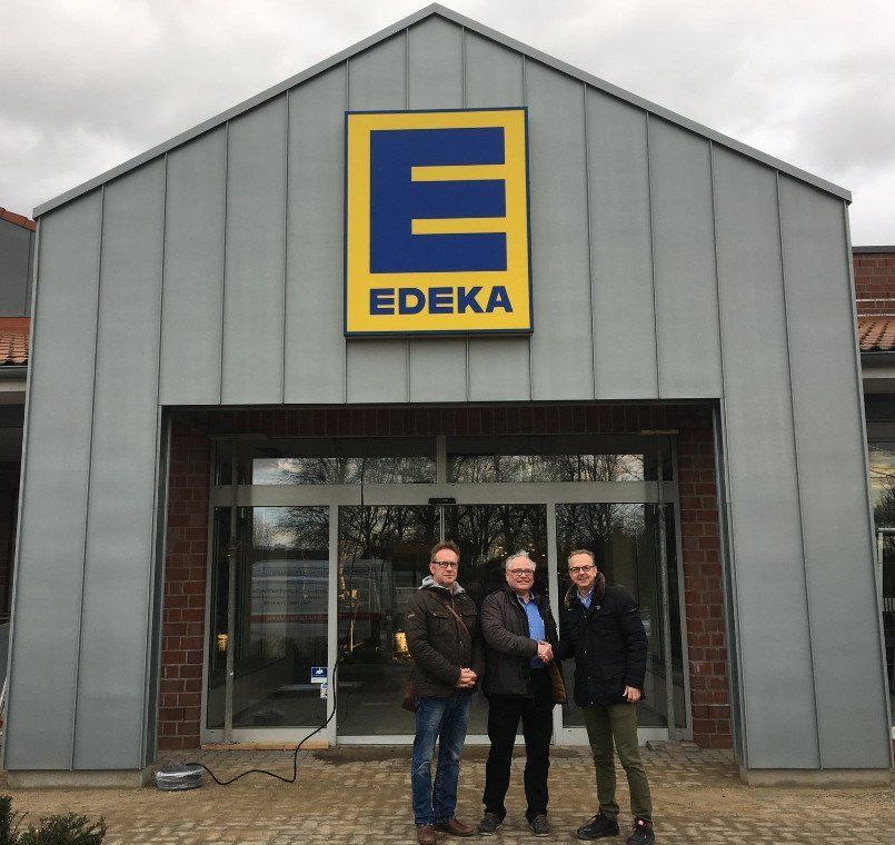 Drei Männer schütteln sich vor dem Eingang eines EDEKA-Lebensmittelgeschäfts die Hände.