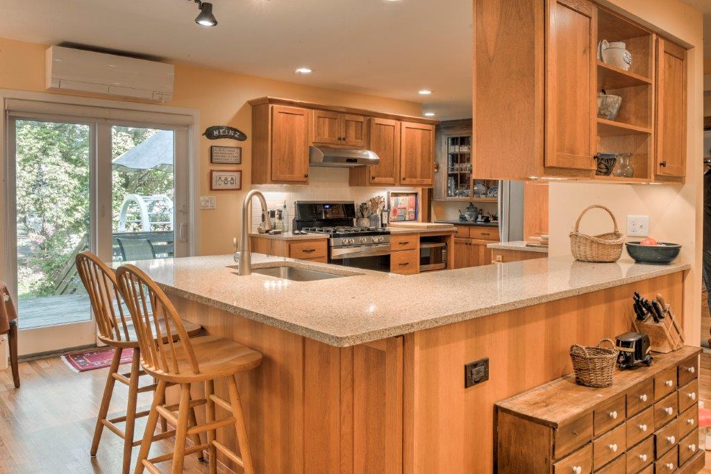 Bright kitchen with wood cabinets, granite island, bar stools, and sliding glass doors to outside.