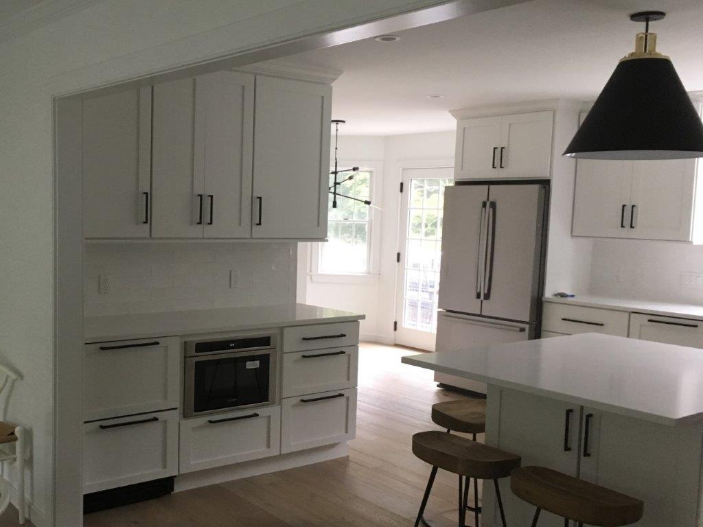 Modern white kitchen with island, stainless fridge, built-in oven, and bright windows