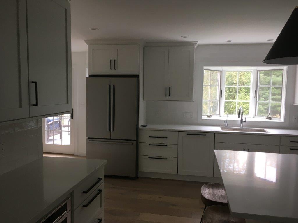 Modern white kitchen with stainless fridge, cabinets, island, and window over the sink
