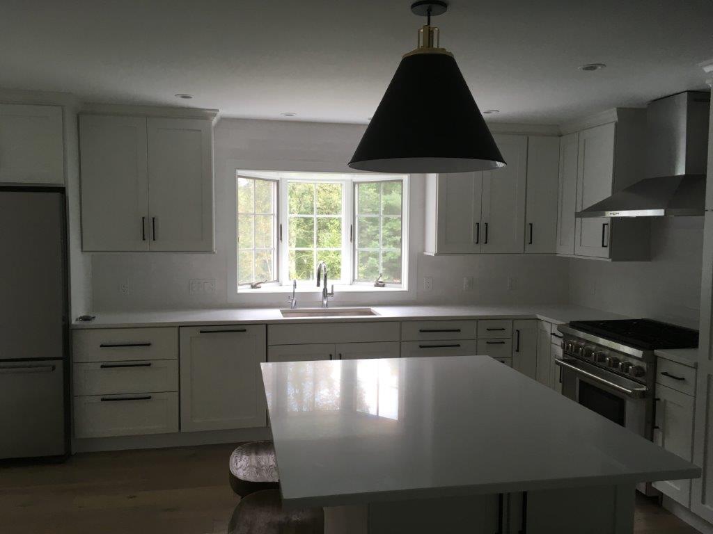 Bright white kitchen with island, cabinets, window over sink, and black pendant light.