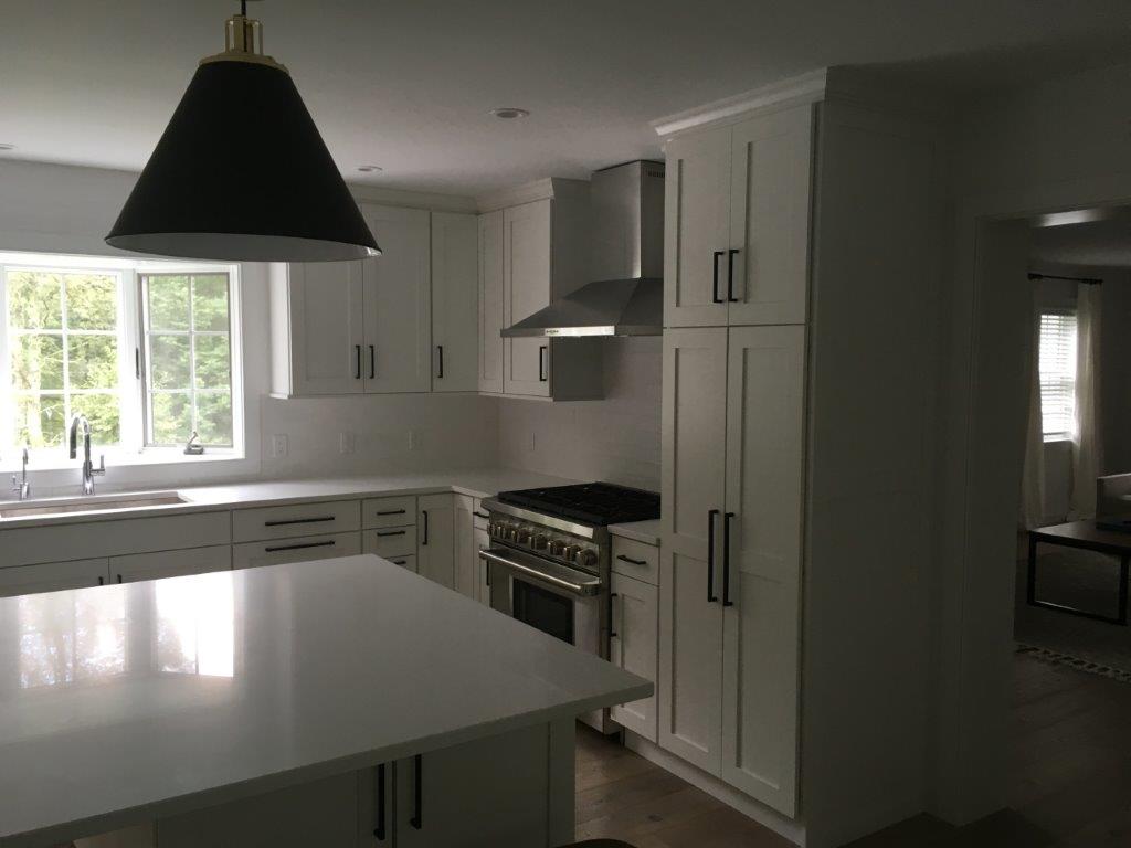 Bright modern kitchen with white cabinets, island, black pendant light, and sunlit window