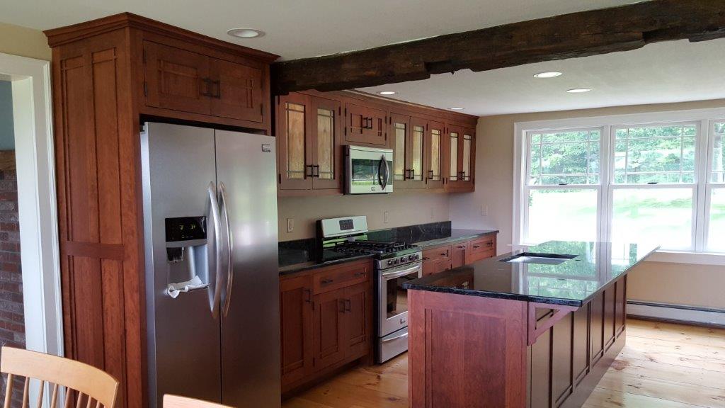 Modern kitchen with stainless fridge, dark wood cabinets, black island, and large windows overlooking a yard
