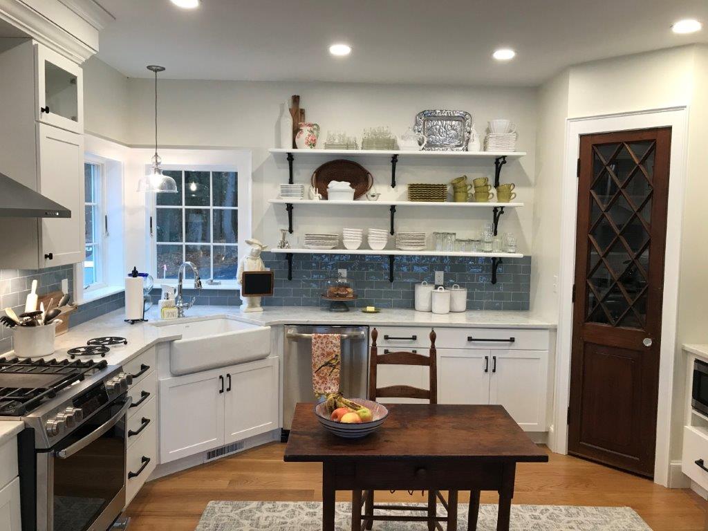Bright kitchen with white cabinets, blue backsplash, wooden table, and dark wood door.