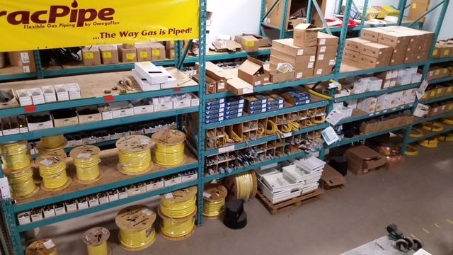 Warehouse shelves stocked with gas piping supplies. Yellow gas lines and various boxed parts are visible.