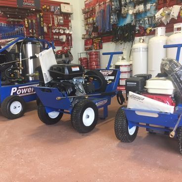 A hardware store interior with three blue pressure washers and propane tanks.