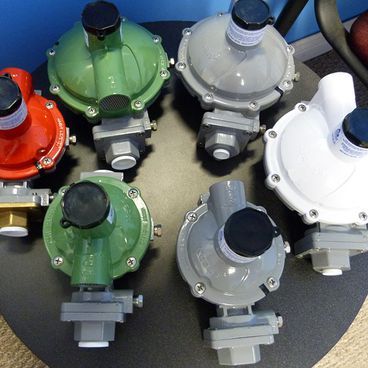 A group of gas regulators in various colors: red, green, gray, and white, arranged on a black surface.
