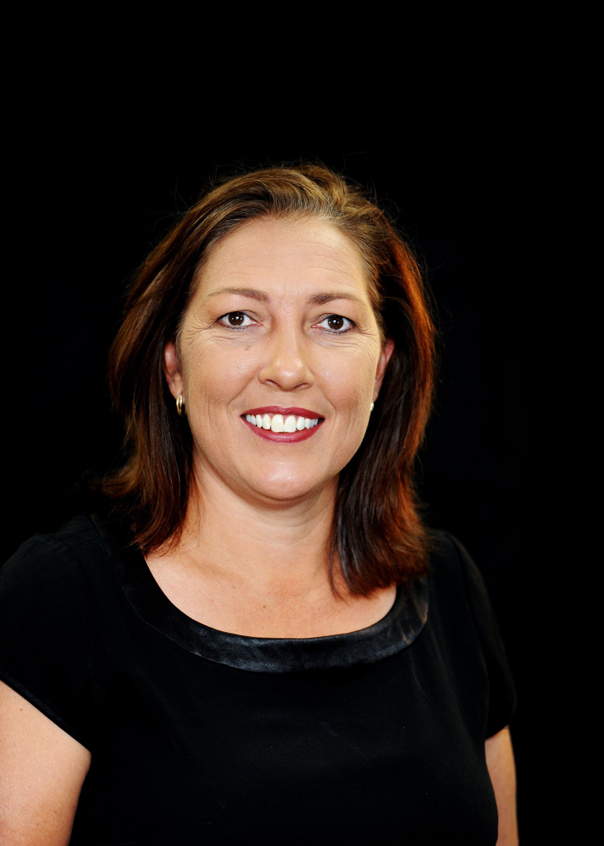 A woman in a black shirt is smiling in front of a black background.