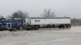 Blue semi-truck pulling a white grain trailer in a snowy parking lot.