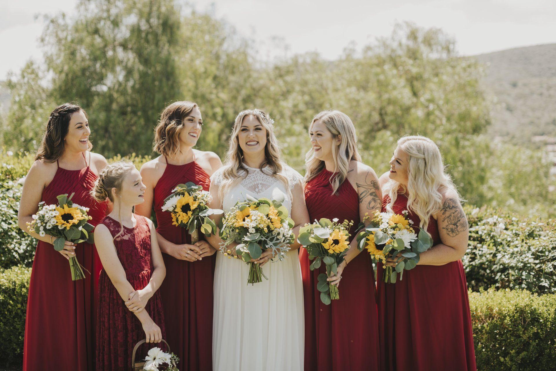 Five bridesmaids in burgundy and ivory dresses holding colorful bouquets outdoors