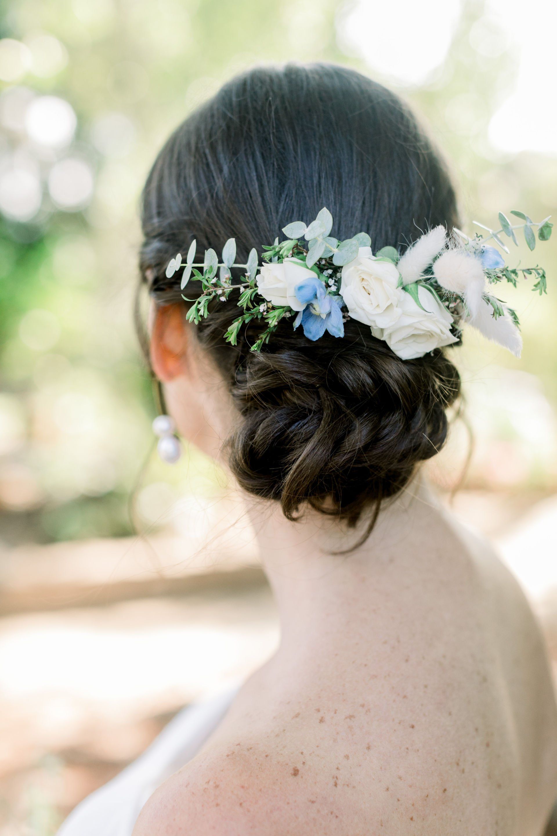 Woman seen from behind with dark hair in a low bun, wearing a white-and-blue floral hairpiece.