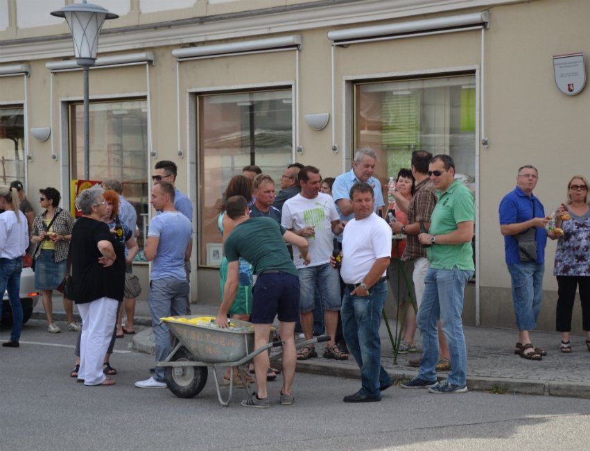 Eine Gruppe von Menschen steht auf einem Bürgersteig, ein Mann schiebt eine Schubkarre