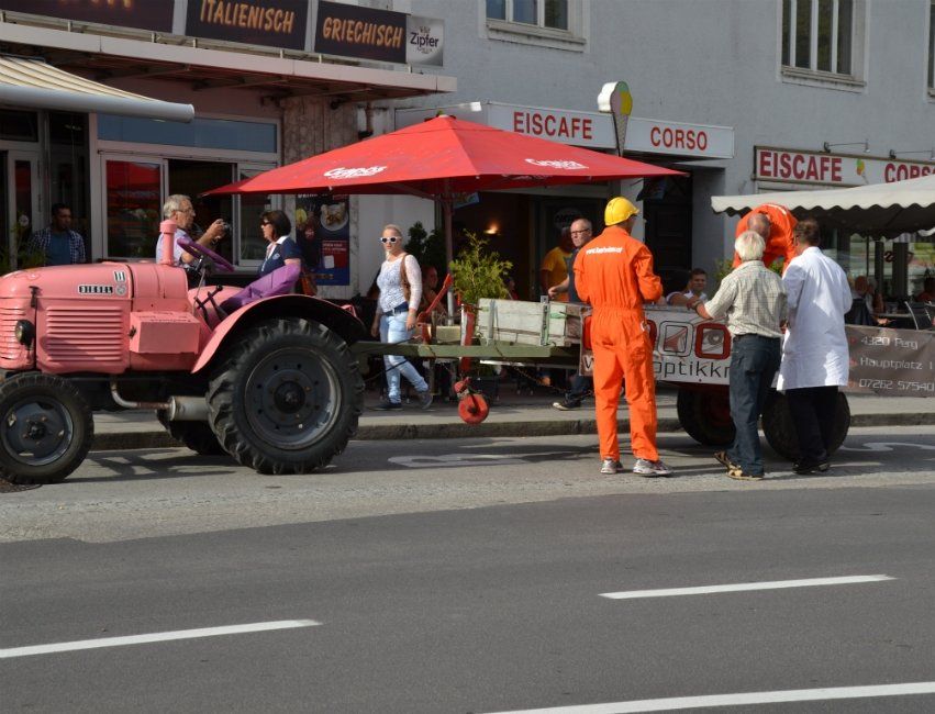 Ein rosa Traktor zieht einen Karren die Straße entlang