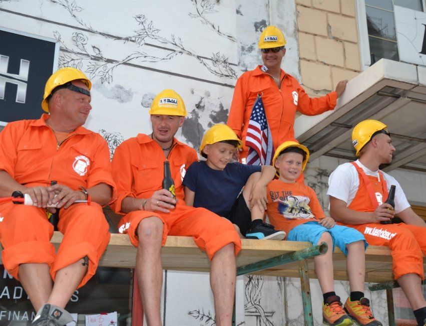 Eine Gruppe von Männern in orangefarbenen Overalls und Schutzhelmen sitzt auf einer Bank