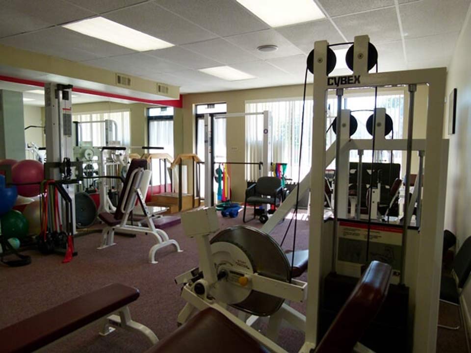 An indoor physical therapy or gym space featuring various workout machines, exercise balls, and a bench.