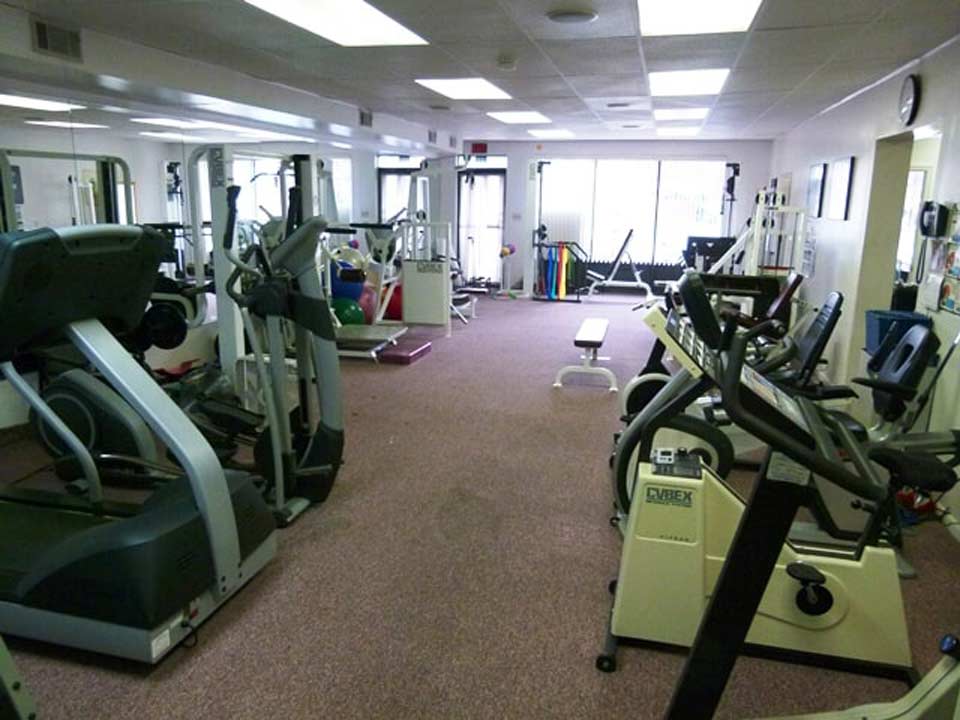 A gym interior with various fitness machines including treadmills and stationary bikes arranged on a carpeted floor.