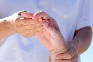 A person in a white top gently holding and examining another person's hand.