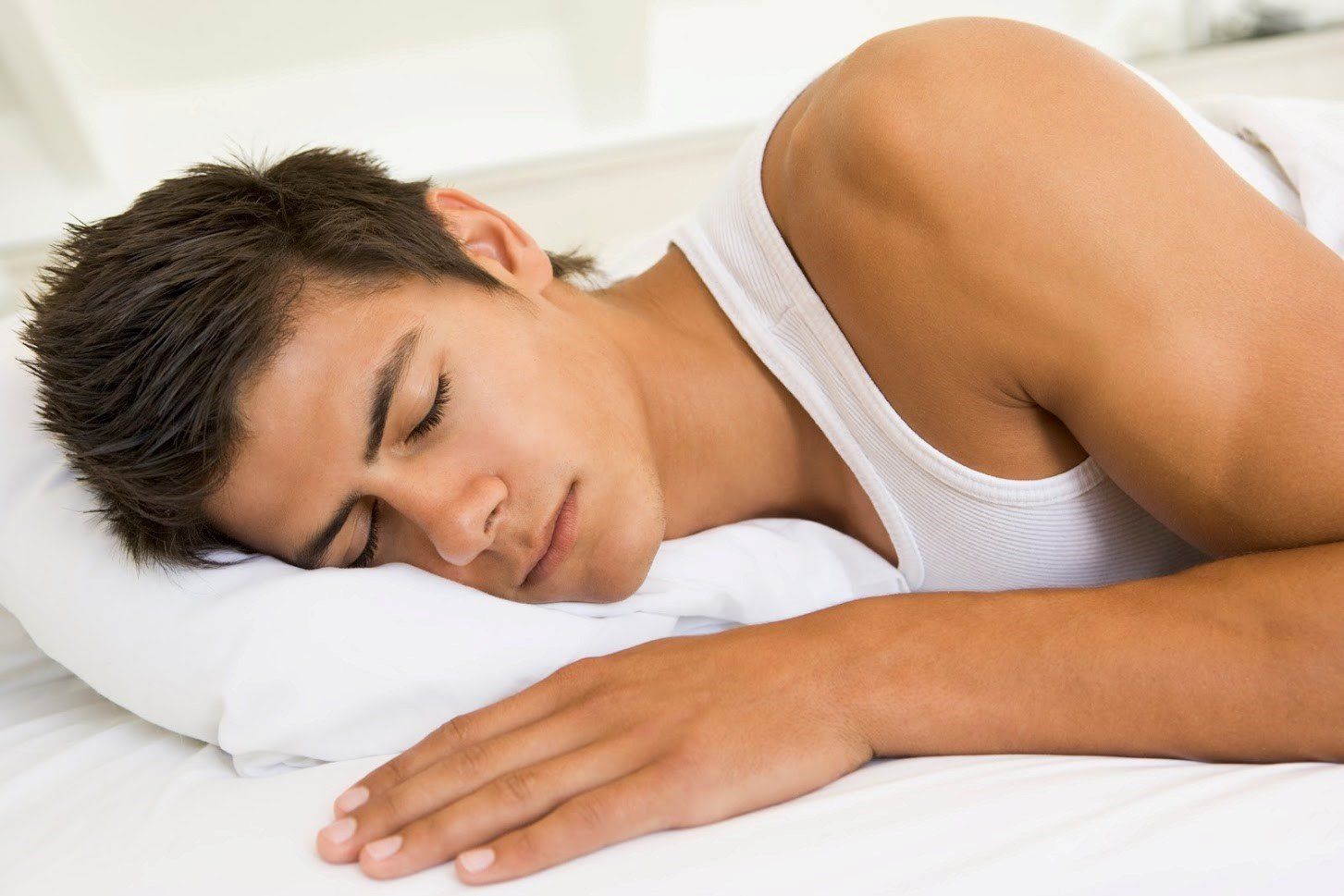 Sleeping Man — Philadelphia, PA — Advanced Physical Therapy A person in a white tank top sleeping peacefully on a white pillow and bed sheets.