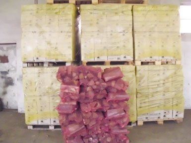 un mucchietto di legna dentro ad una rete rossa e dietro dei bancali con delle scatole coperte da una plastica gialla