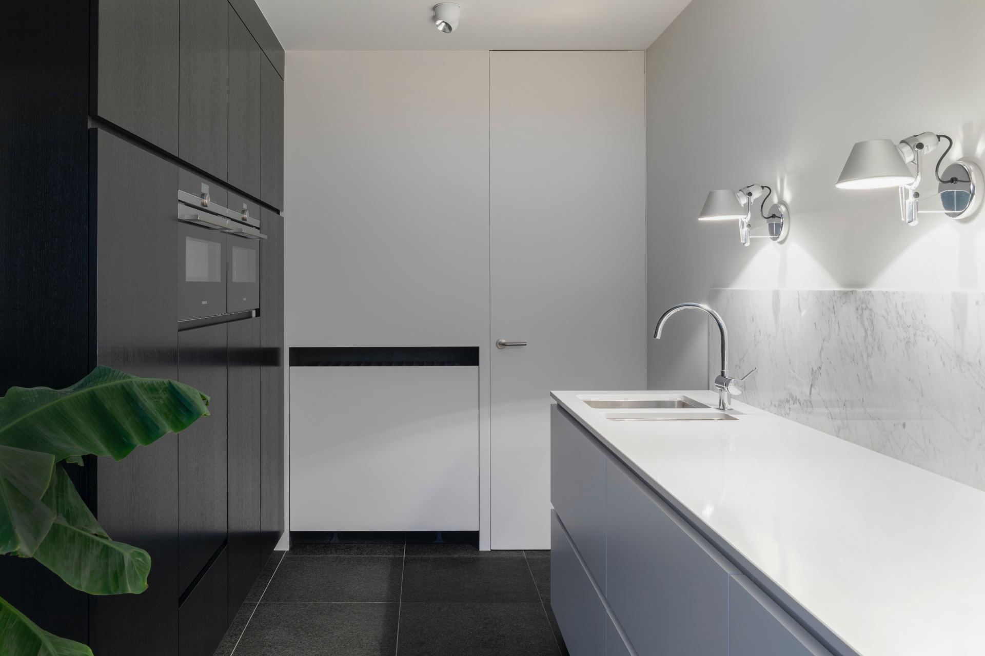 A kitchen with black cabinets , white counter tops , and a sink.