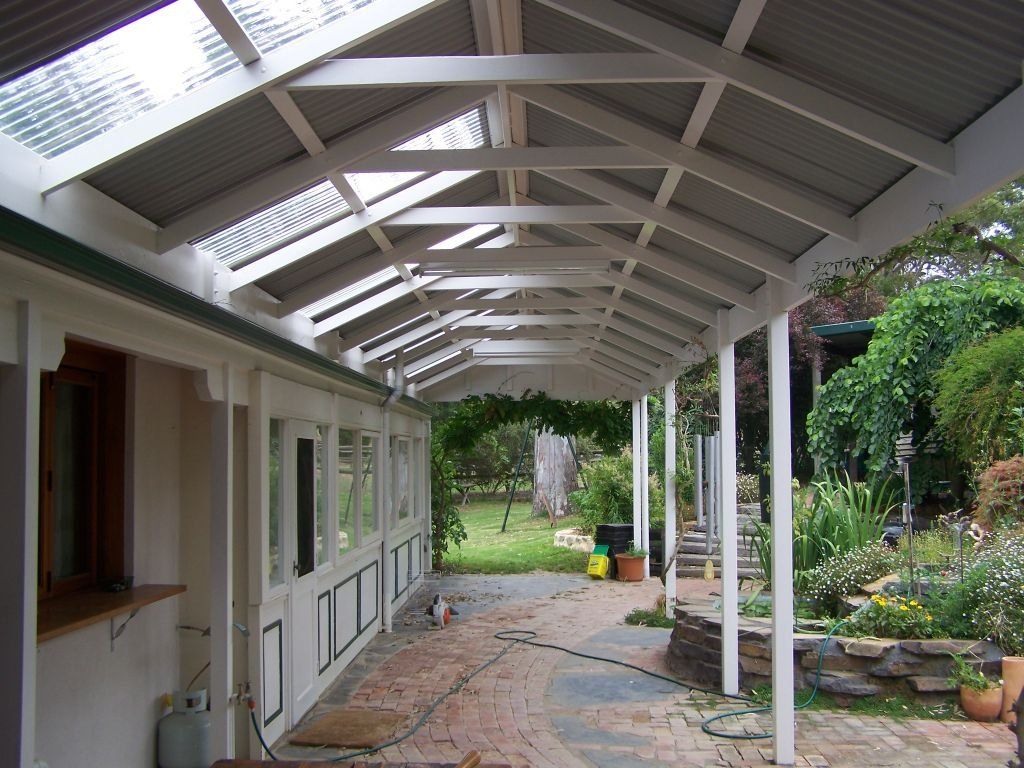 Covered outdoor patio with a pitched roof, skylights and white timber beams beside a landscaped garden.