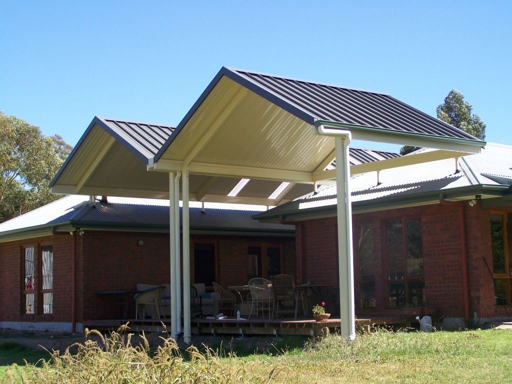Covered outdoor patio with twin pitched metal roofs attached to a brick home.