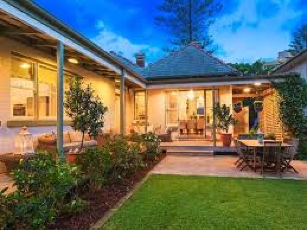 Renovated home with a covered outdoor entertaining area, landscaped garden and patio dining space at dusk.