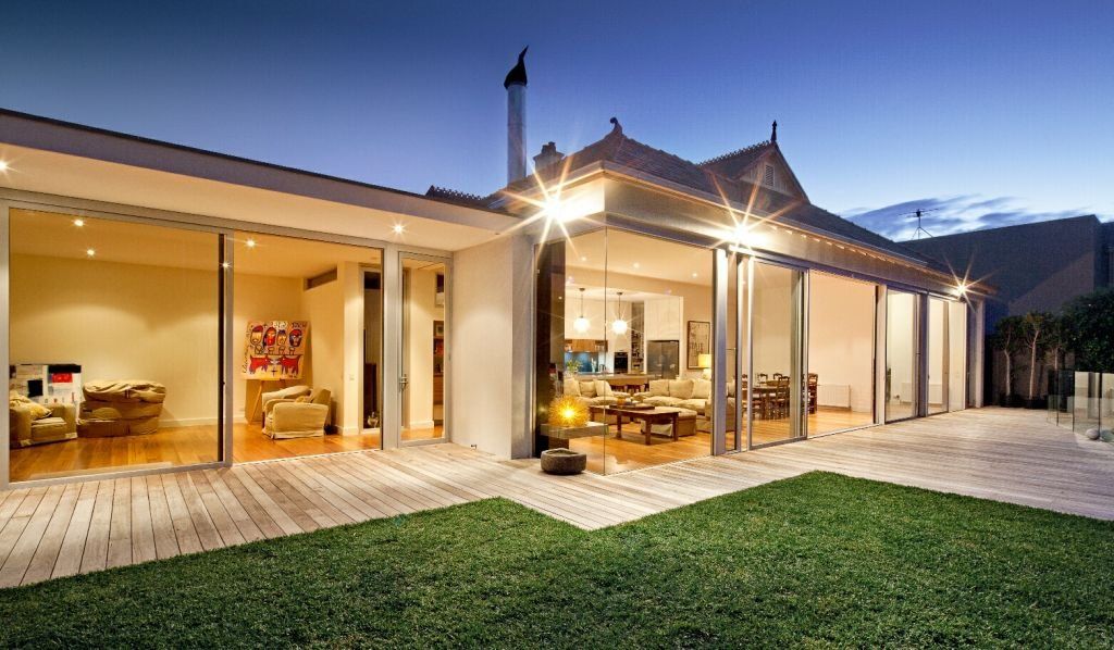Modern home extension with large glass doors and timber decking at dusk.