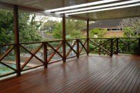 Covered timber deck with wooden balustrades overlooking a leafy garden.