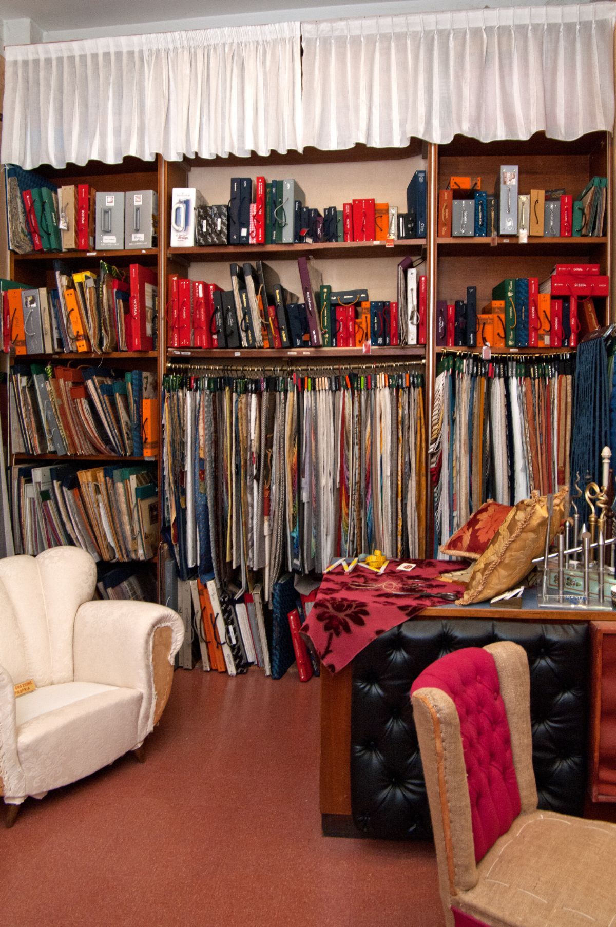Un negozio di campioni di tessuto presenta scaffali con libri ben organizzati e campioni di tessuto appesi, con due sedie in primo piano.