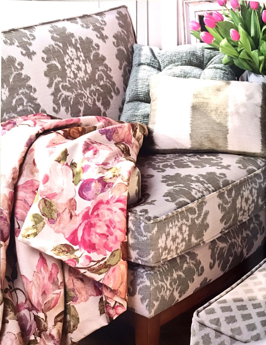 Una sedia decorata con una coperta a fiori, un cuscino decorativo dalla texture particolare e un vaso di tulipani rosa nelle vicinanze.