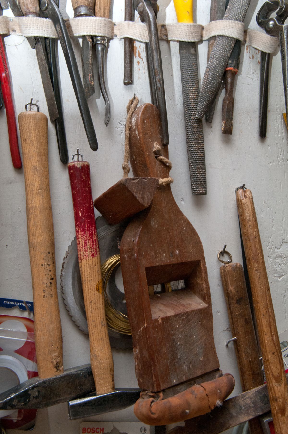 Una rastrelliera a muro che contiene vari utensili manuali d'epoca, tra cui martelli con manico in legno, lime e una pialla a mano in legno.