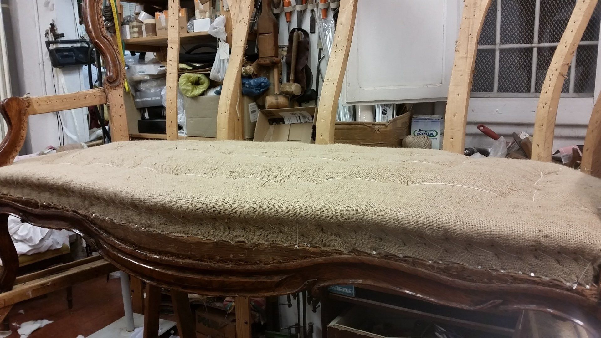 In un laboratorio disordinato si trova una struttura di legno per mobili, attualmente in fase di rivestimento con tessuto beige.