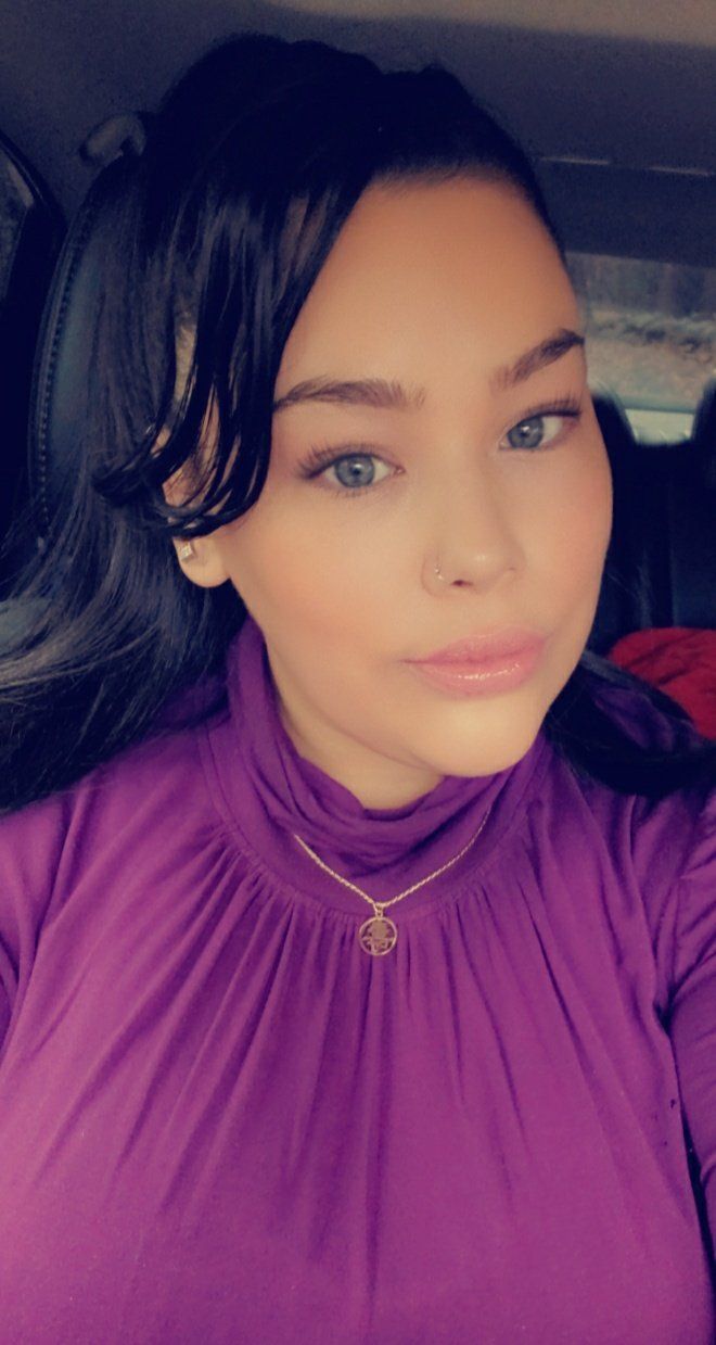 Woman with dark hair in a purple turtleneck. She wears a gold necklace and looks at the camera.