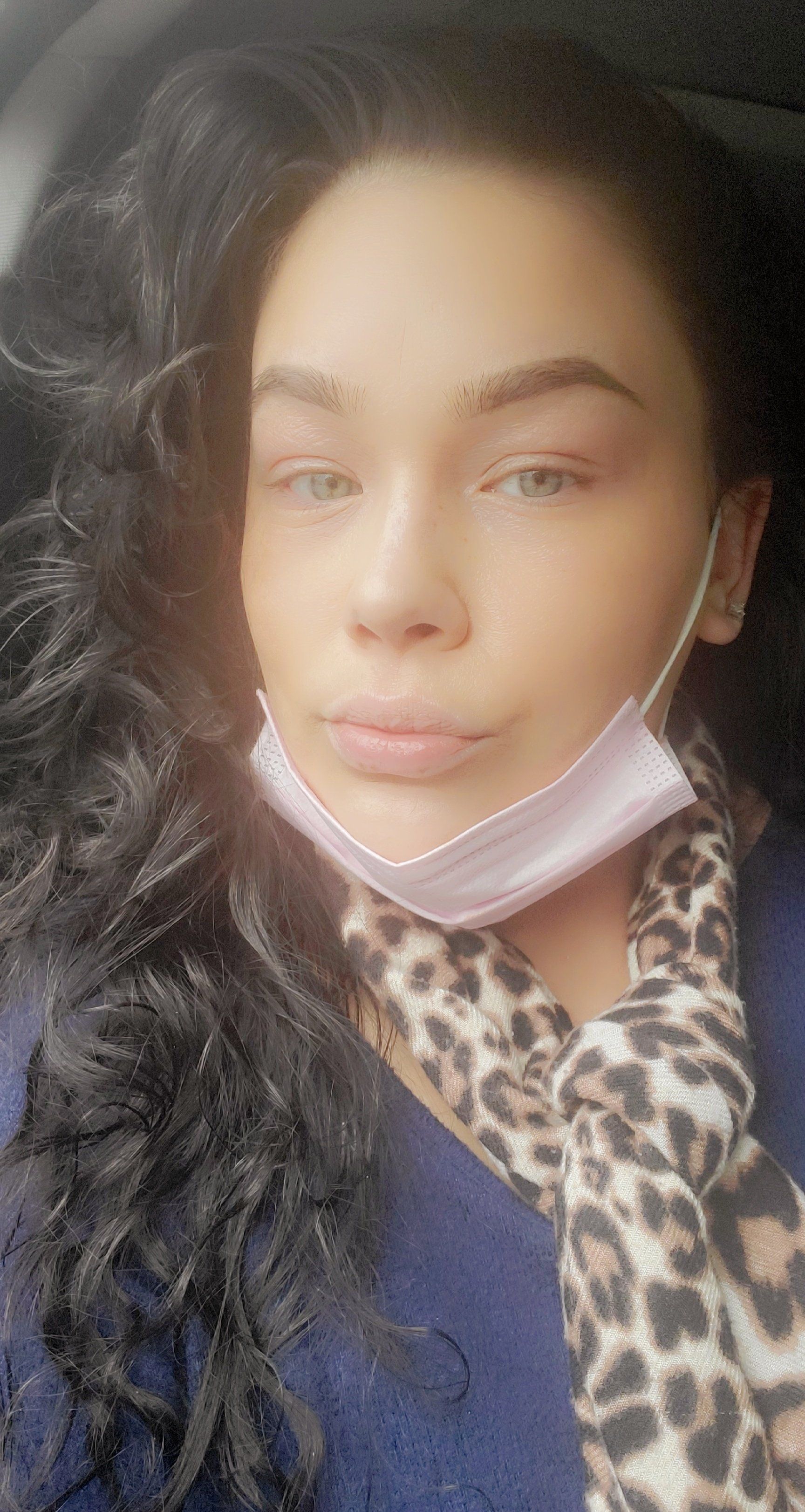 Woman with dark curly hair and light eyes, wearing a mask and leopard print scarf.