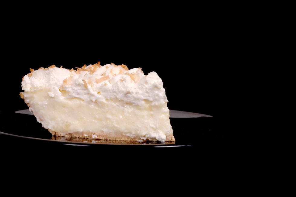 A slice of coconut pie on a black plate on a black background.