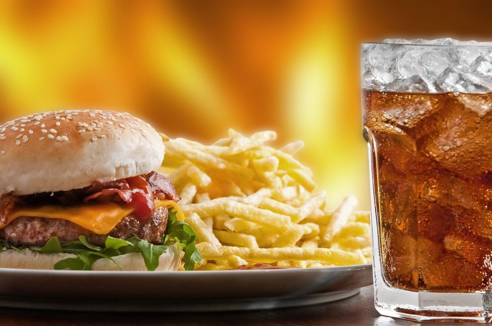 A plate of hamburger and french fries next to a glass of soda.