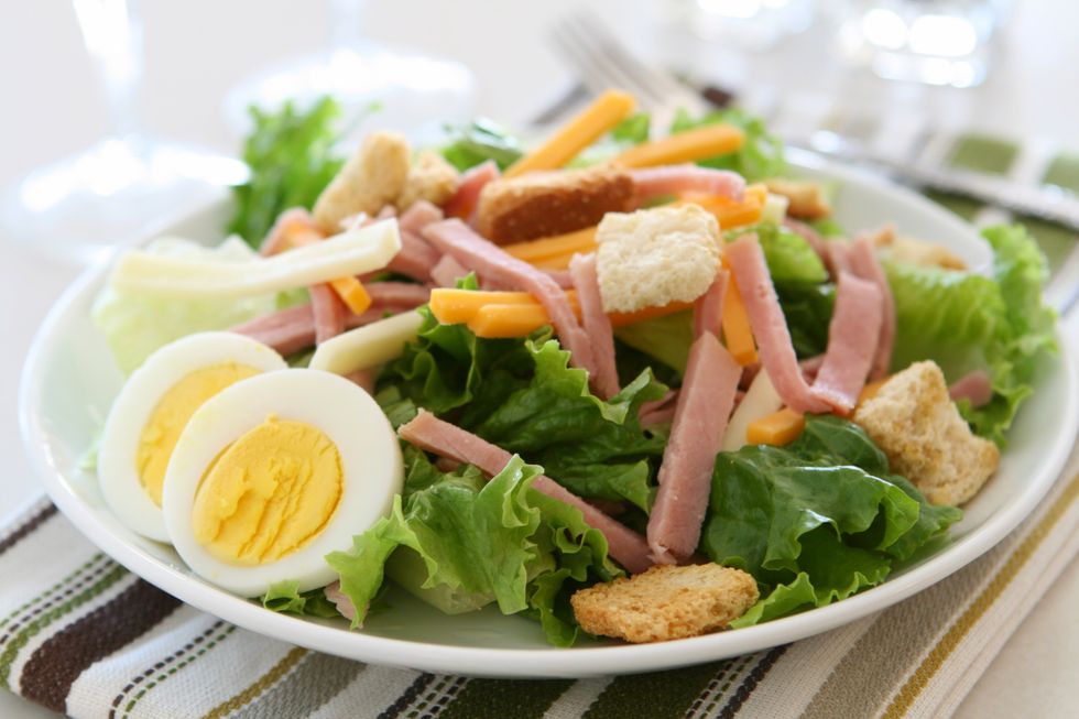 A salad with ham , eggs , croutons and cheese on a plate.