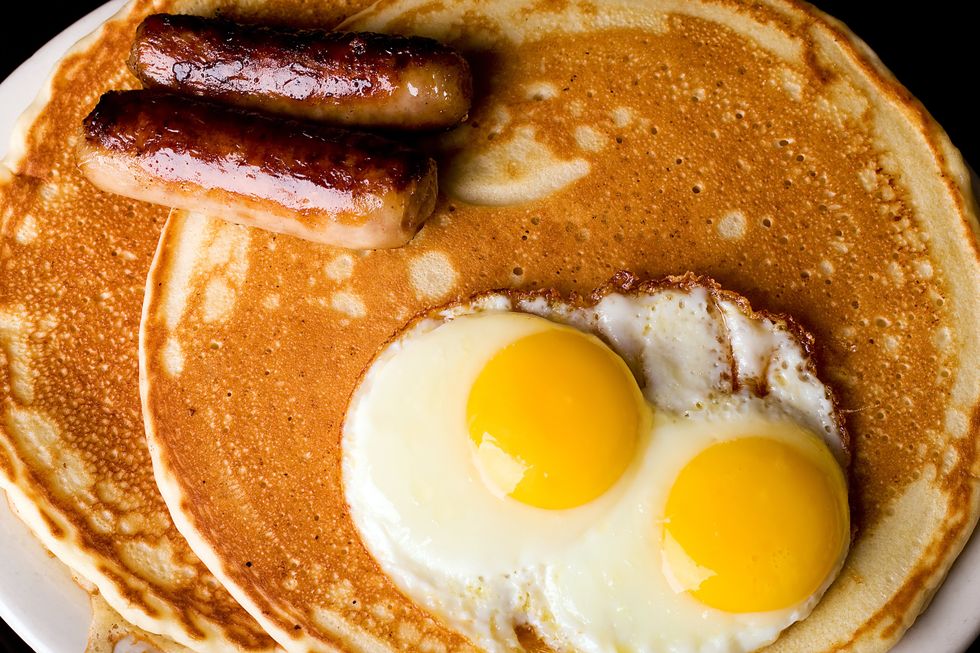 A plate of pancakes with eggs and sausages on it