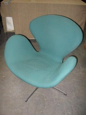 A blue chair with a swan shaped back sits on a concrete floor
