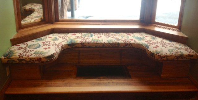 A wooden window seat with a floral cushion in front of a window.