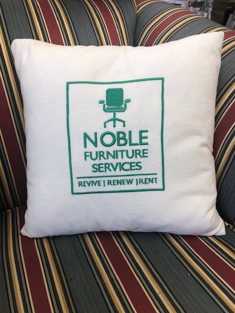 A noble furniture services pillow sits on a striped couch
