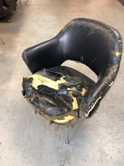 A black chair with a broken seat is sitting on a concrete floor.
