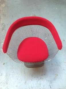 A wire chair with a red cushion is sitting on a concrete floor.