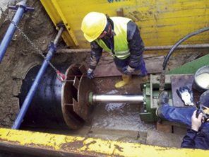 A man in a yellow hard hat is working on a machine in the dirt.