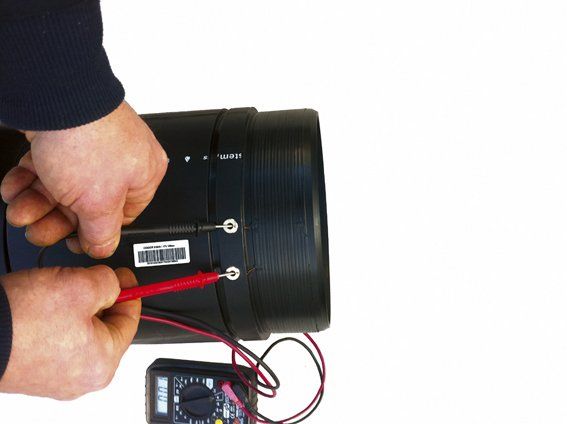 A person is using a multimeter to test a black pipe