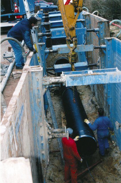Two men are working on a large pipe in a trench