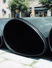A bunch of black pipes are stacked on top of each other on the sidewalk.